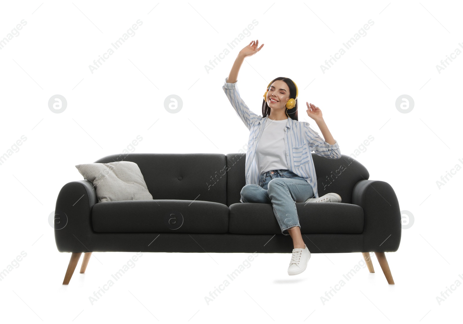 Photo of Young woman listening to music on comfortable grey sofa against white background