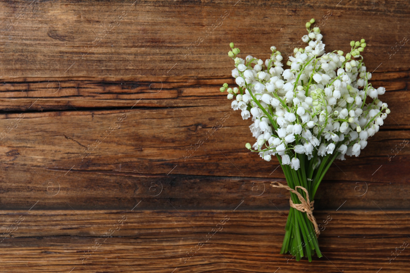 Photo of Beautiful lily of the valley flowers on wooden table, top view. Space for text