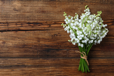 Photo of Beautiful lily of the valley flowers on wooden table, top view. Space for text