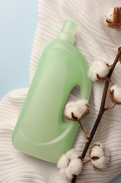 Photo of Bottle of fabric softener, white knitted cloth and cotton flowers on light background, flat lay