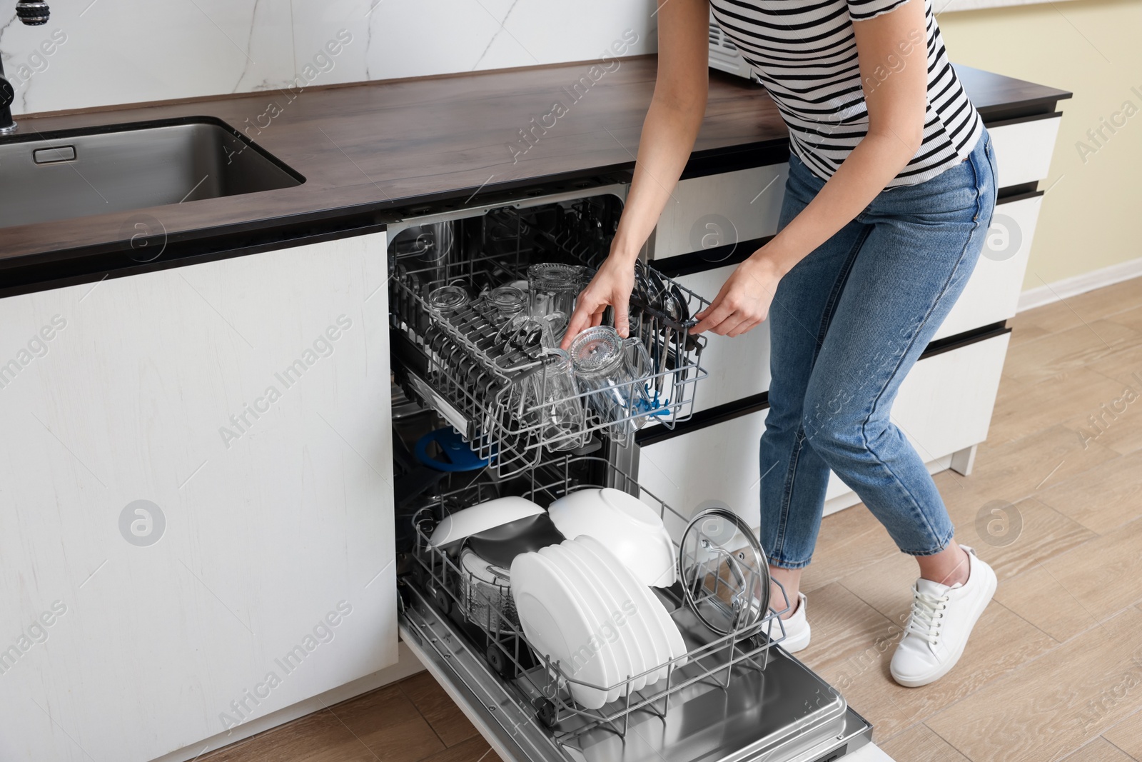 Photo of Woman loading dishwasher with glasses and plates in kitchen, closeup