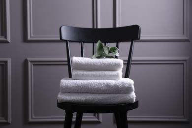 Photo of Stacked soft towels and green leaves on black chair indoors