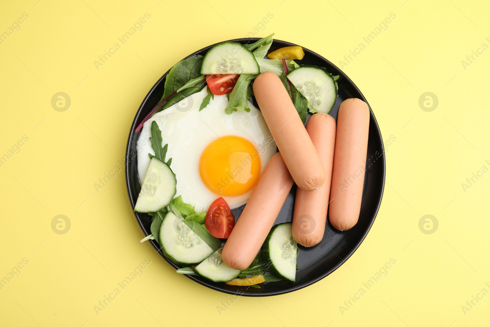 Photo of Delicious breakfast with boiled sausages and fried egg on yellow background, top view