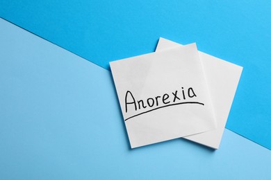 Note papers with word Anorexia on light blue background, flat lay. Space for text