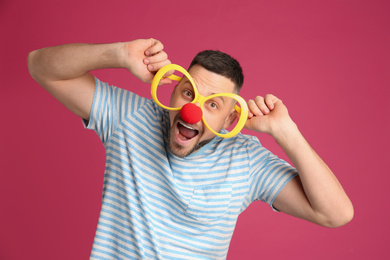 Photo of Funny man with large glasses and clown nose on pink background. April fool's day