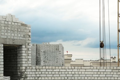 Photo of Construction site with tower crane near unfinished walls and buildings under cloudy sky