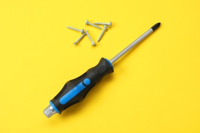 Photo of Screwdriver with black handle and screws on yellow background, flat lay