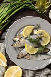 Photo of Fresh raw sprats, green onion, cut lemon and dill on wooden table, flat lay