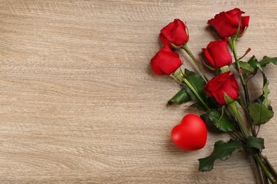 Beautiful red roses and decorative heart on wooden background, flat lay with space for text. Valentine's Day celebration