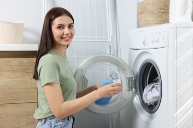 Photo of Woman pouring fabric softener from bottle into cap near washing machine in bathroom