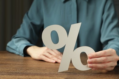 Photo of Woman holding percent sign at wooden table, closeup