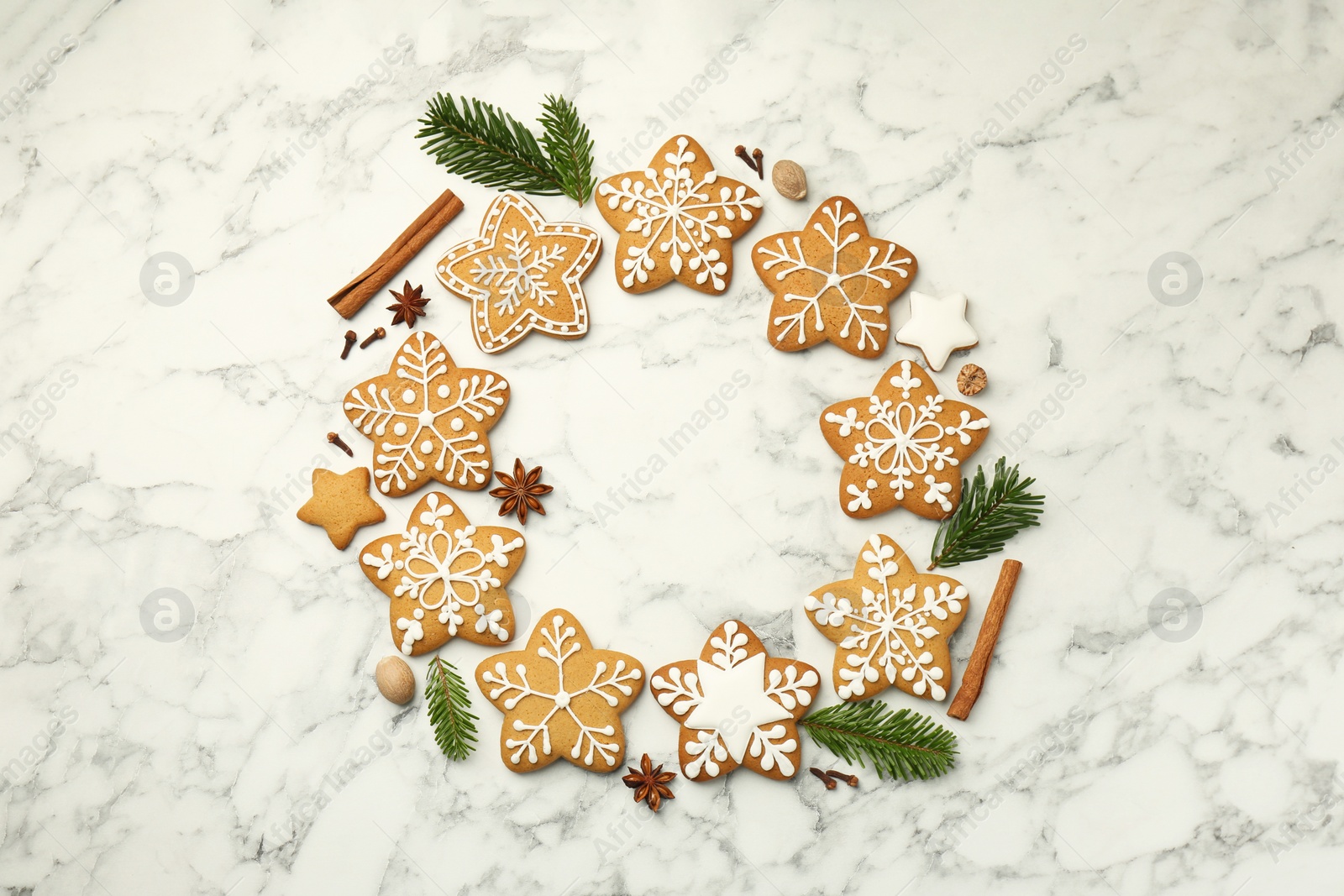 Photo of Tasty star shaped Christmas cookies with icing, spices and fir tree twigs on white marble table, flat lay. Space for text