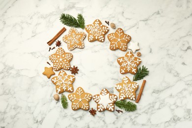 Photo of Tasty star shaped Christmas cookies with icing, spices and fir tree twigs on white marble table, flat lay. Space for text