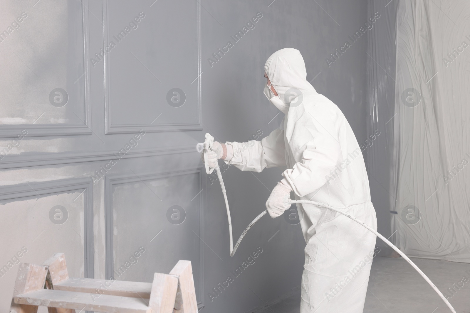 Photo of Decorator dyeing wall in grey color with spray paint indoors