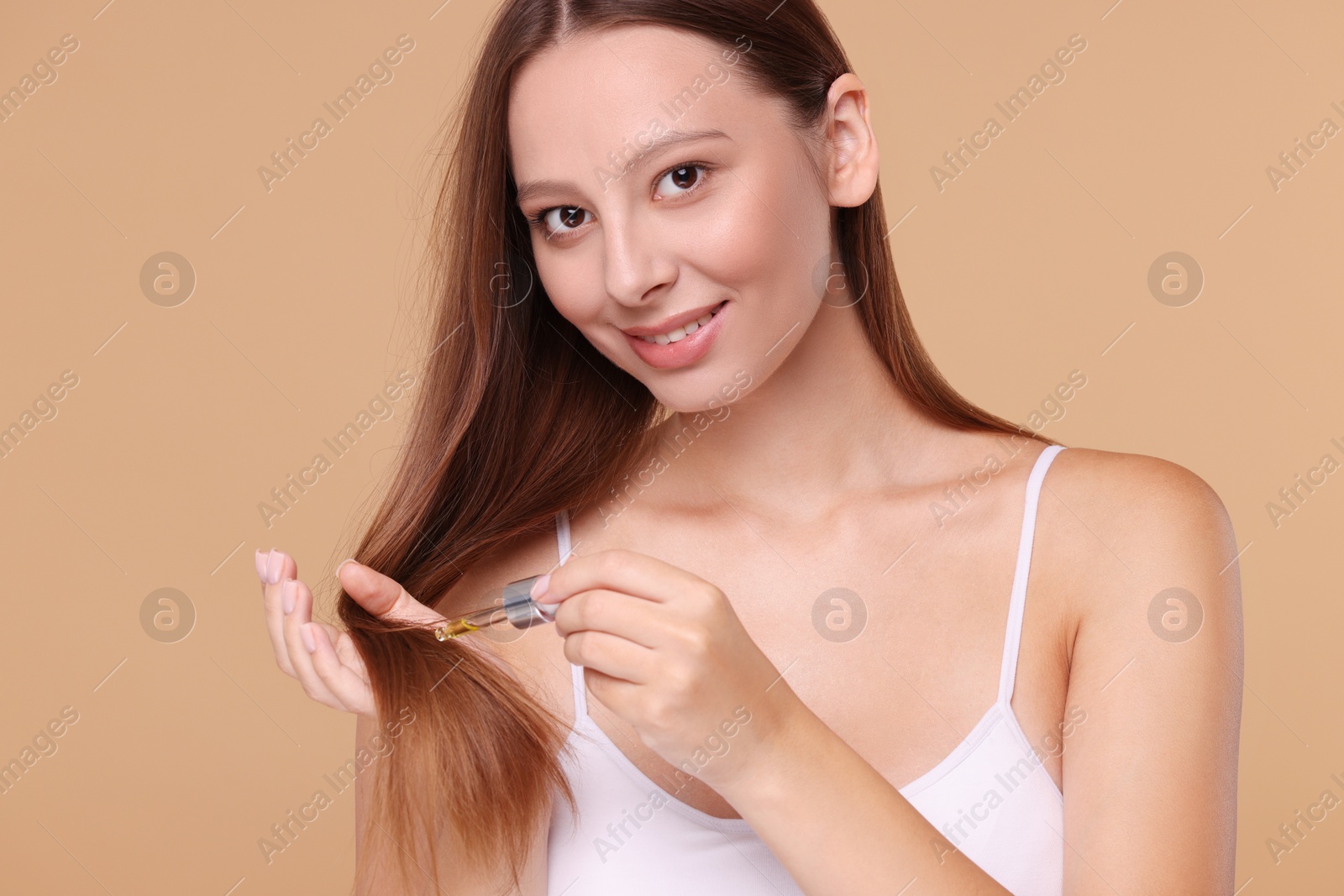 Photo of Beautiful woman applying serum onto hair on beige background