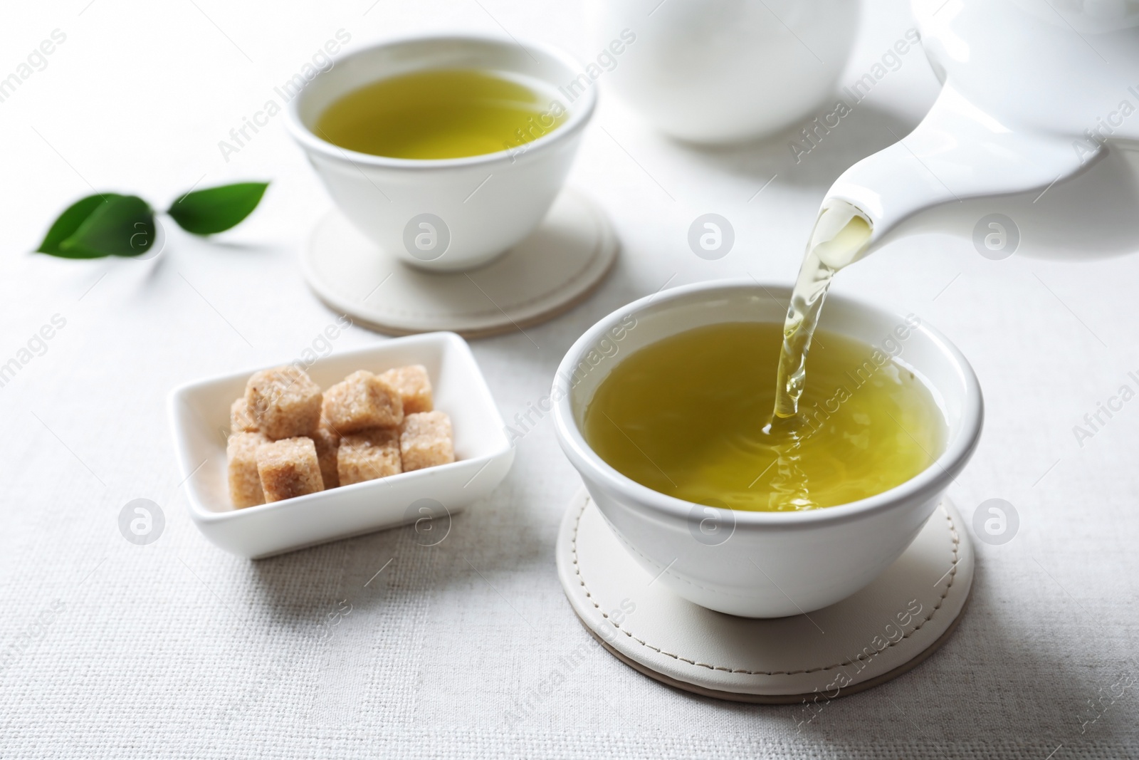 Photo of Pouring green tea into white porcelain cup on light table