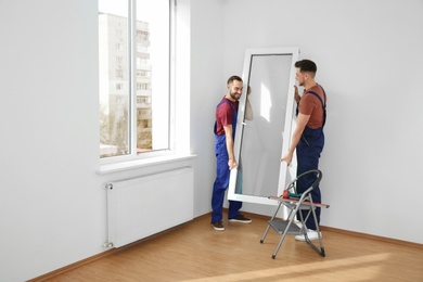 Construction workers installing plastic window in house