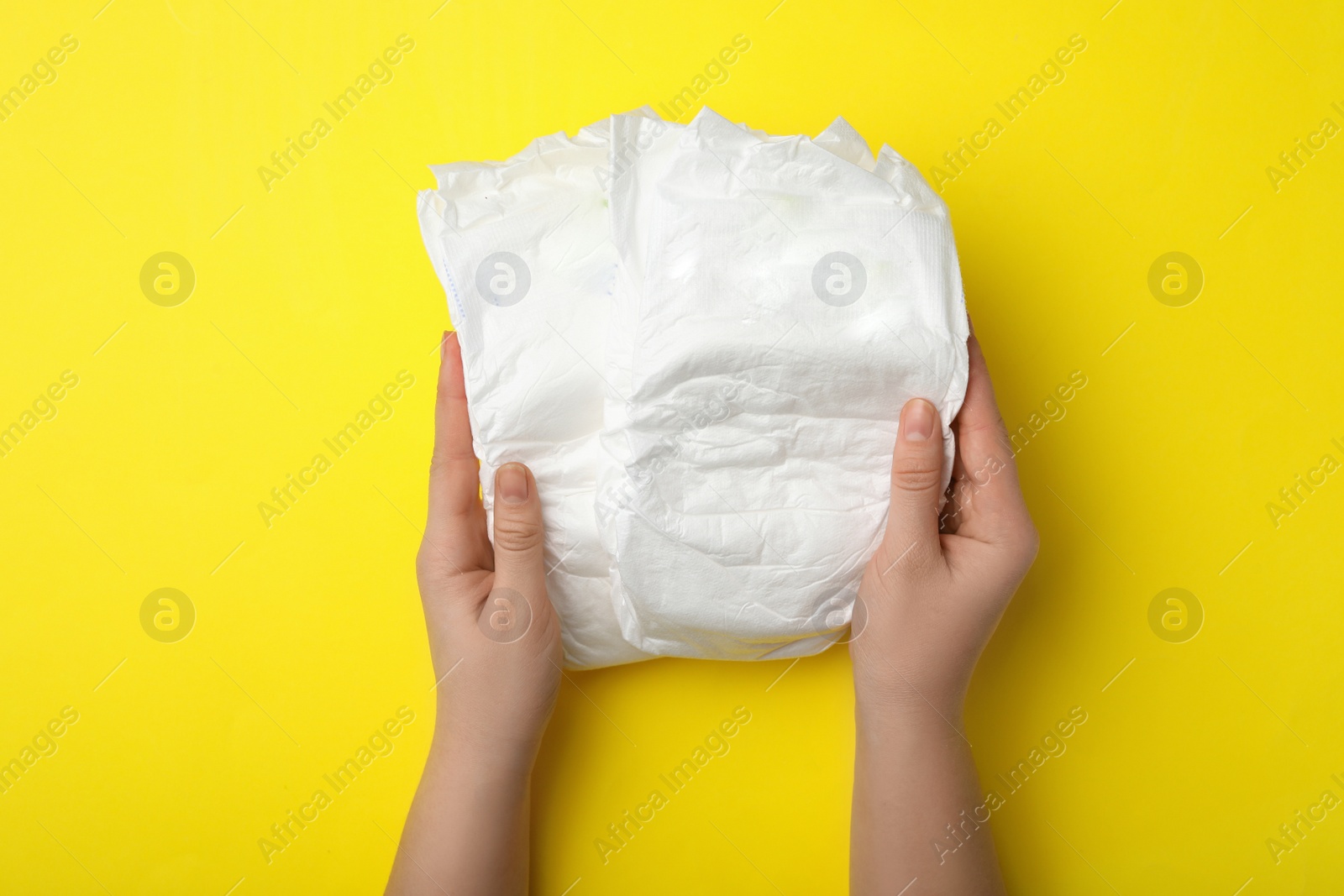 Photo of Woman with diapers on yellow background, closeup