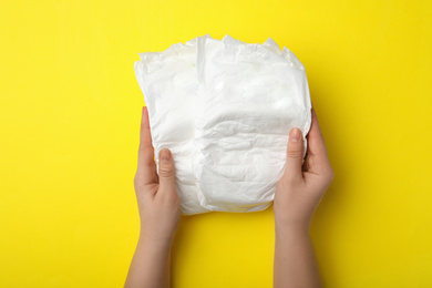 Woman with diapers on yellow background, closeup