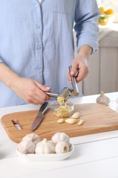 Woman squeezing garlic with press at white wooden table indoors, closeup