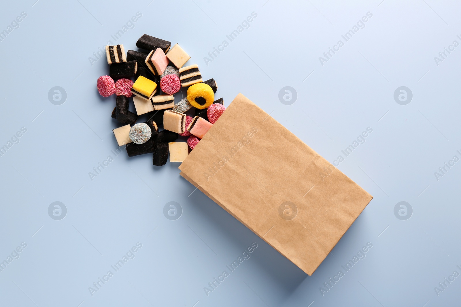 Photo of Paper bag with tasty liquorice candies on light blue background, top view