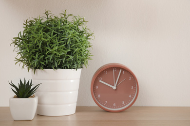 Wooden shelf with beautiful plants and clock on light wall