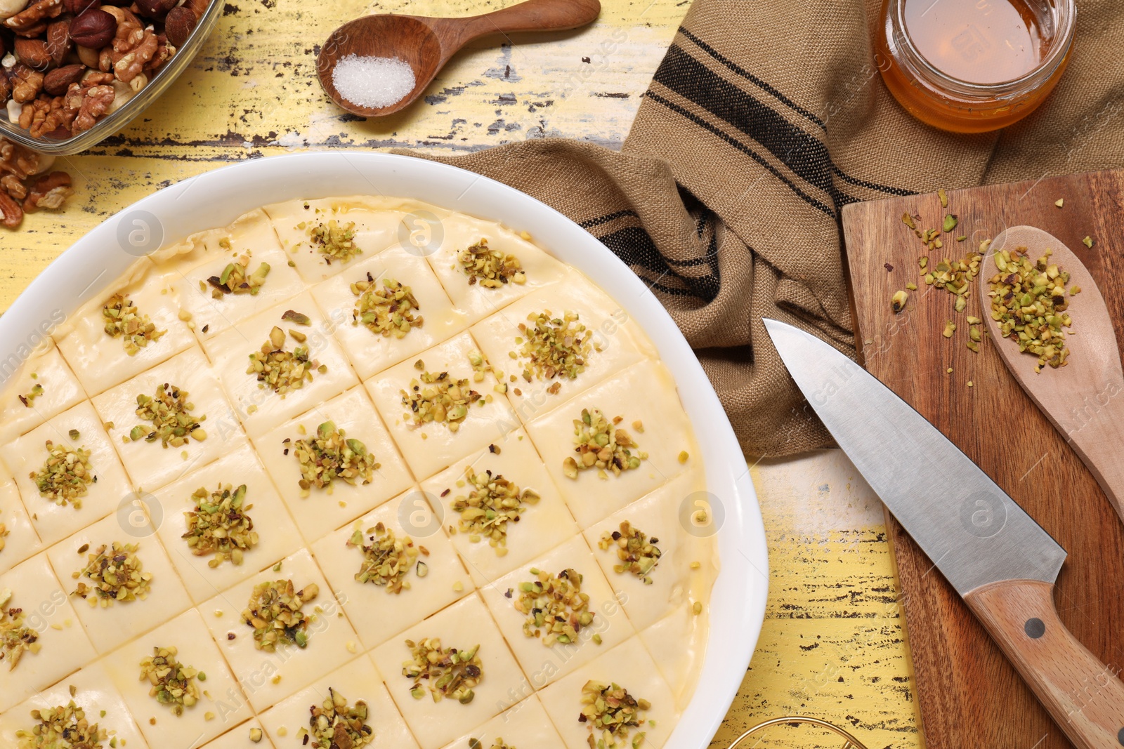 Photo of Making delicious baklava. Raw dough with ingredients on yellow wooden table, flat lay