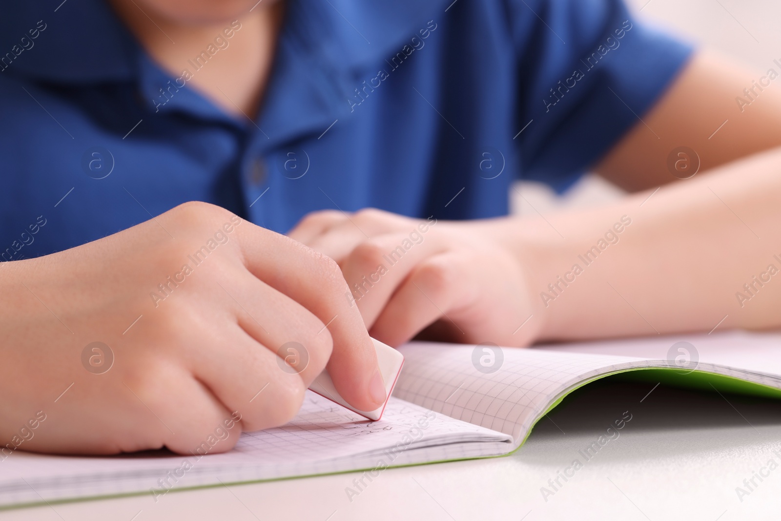 Photo of Boy erasing mistake in his notebook at white desk, closeup