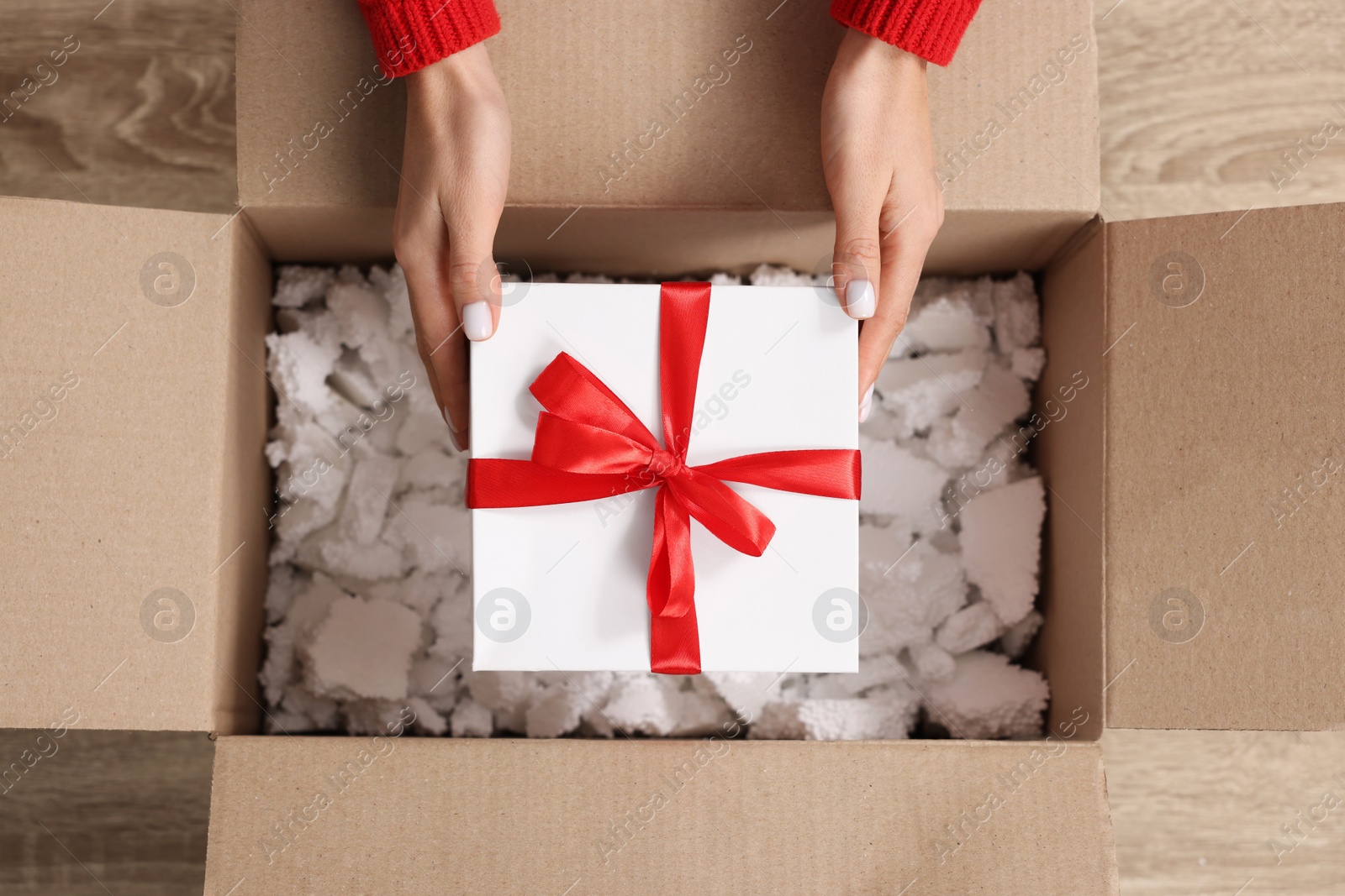 Photo of Woman putting Christmas gift box into parcel at wooden table, top view. Sending present by mail