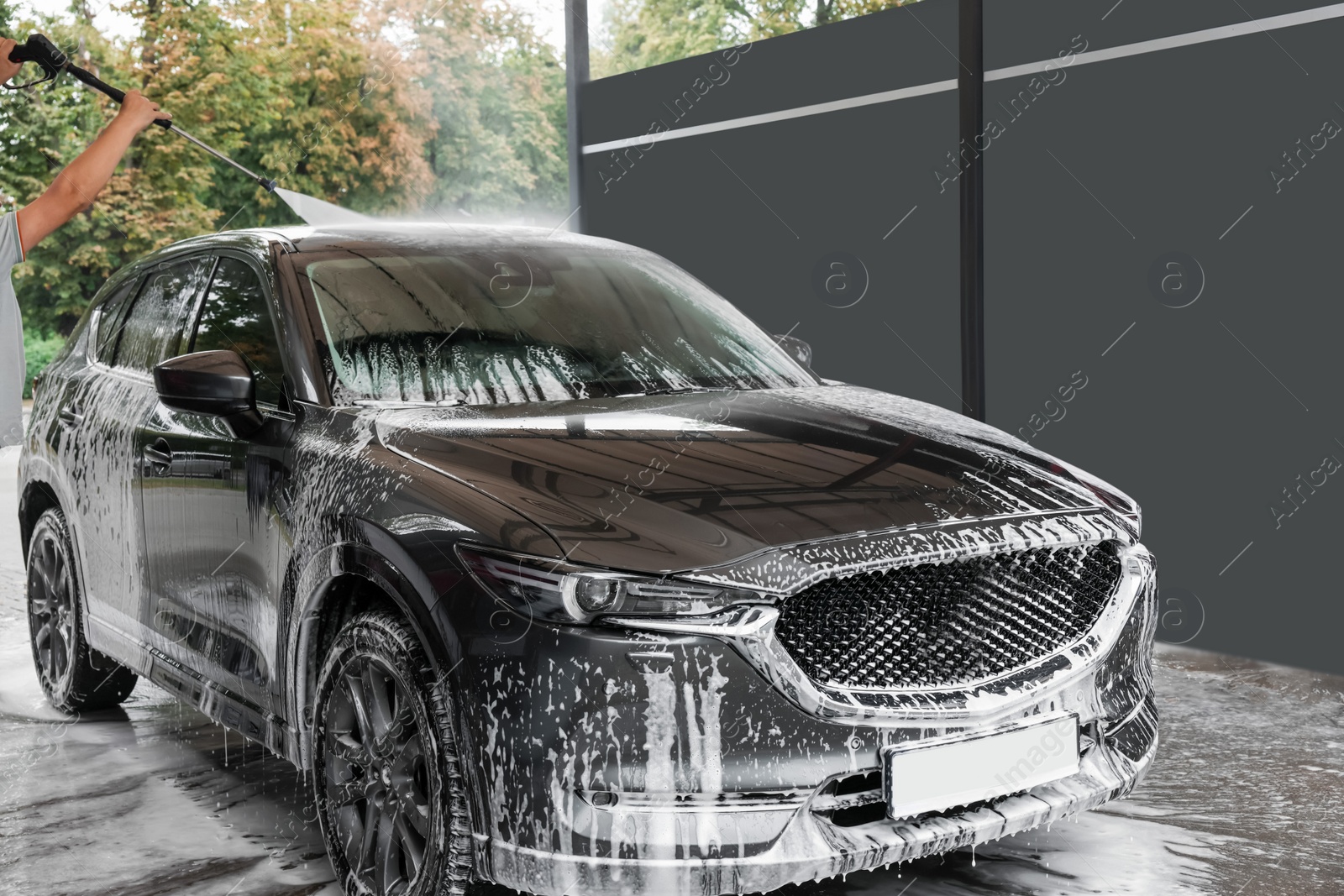 Photo of Man washing auto with high pressure water jet at car wash, closeup