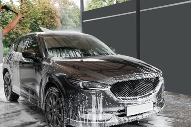 Photo of Man washing auto with high pressure water jet at car wash, closeup