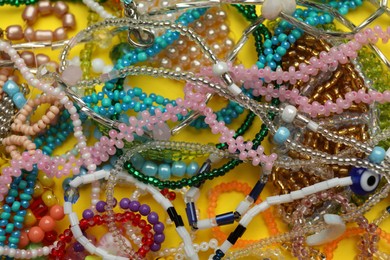 Photo of Pile of beautiful handmade beaded jewelry on yellow background, closeup