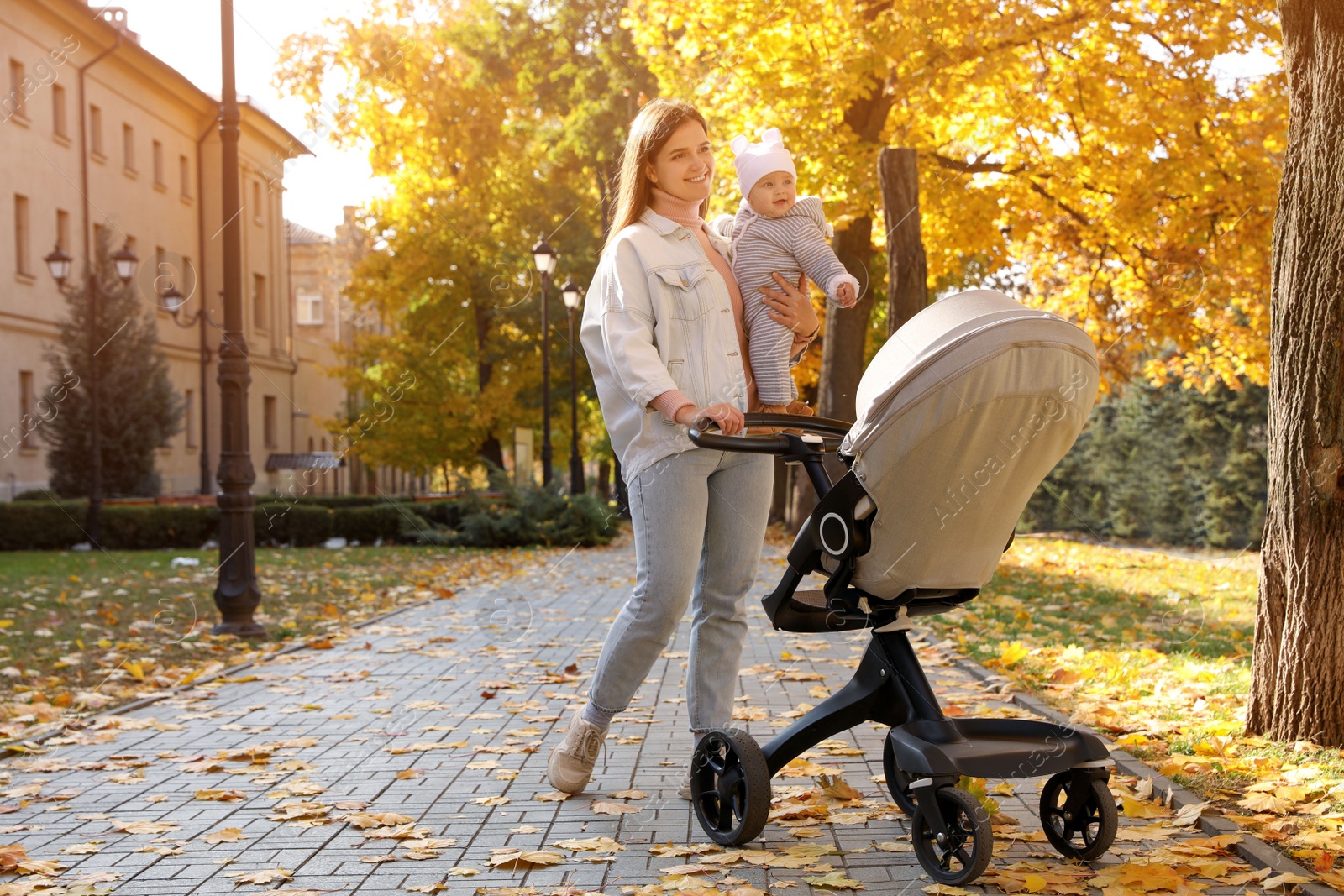 Photo of Happy mother walking with her baby daughter and stroller outdoors on sunny autumn day, space for text