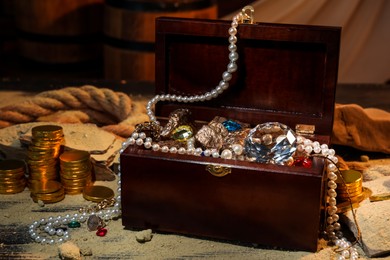 Photo of Chest with treasures and scattered sand on wooden table