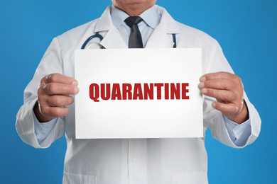 Image of Doctor holding sign with text QUARANTINE on blue background, closeup. Stay at home during coronavirus outbreak