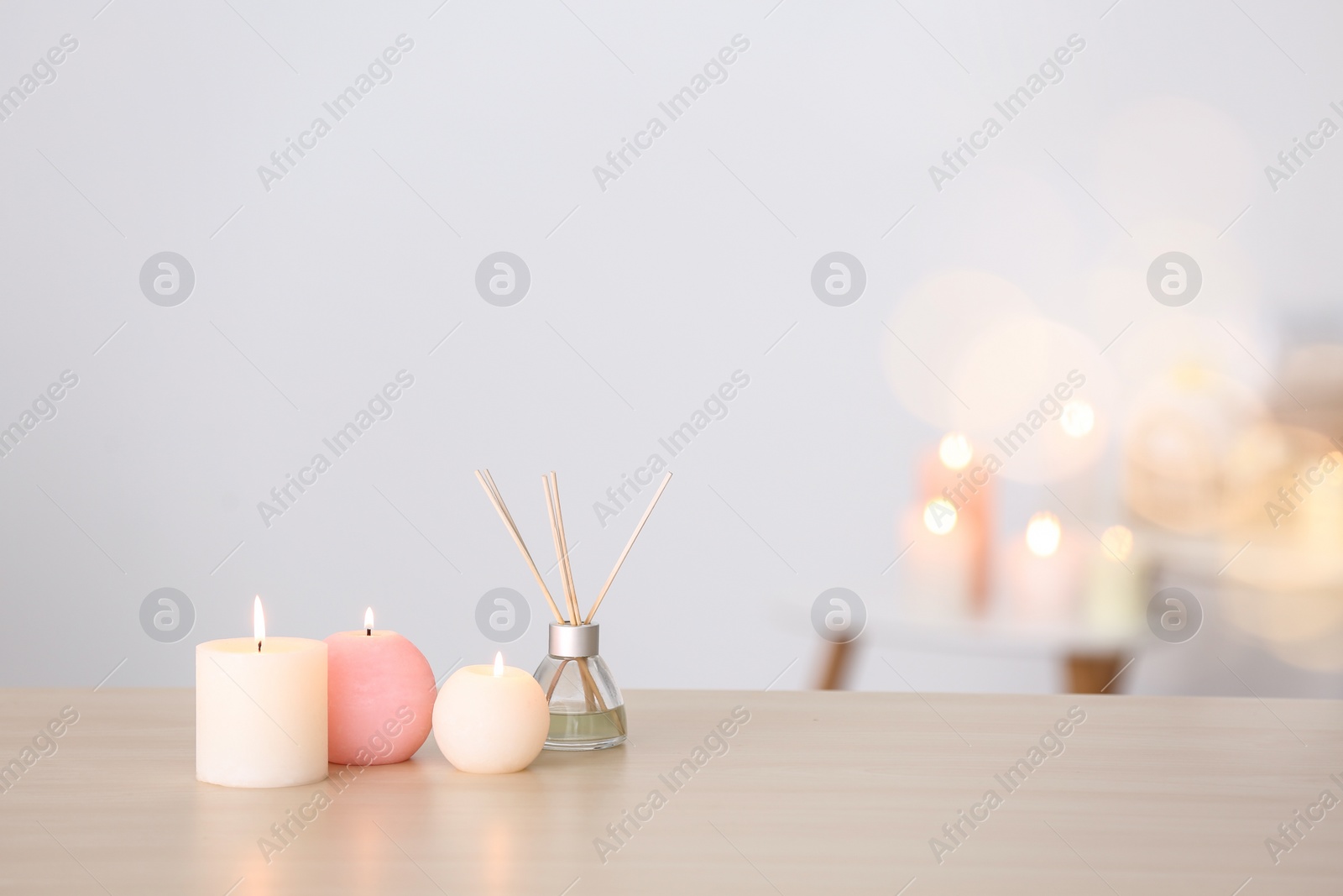 Photo of Candles and reed air freshener on table against blurred background, space for text. Spa concept