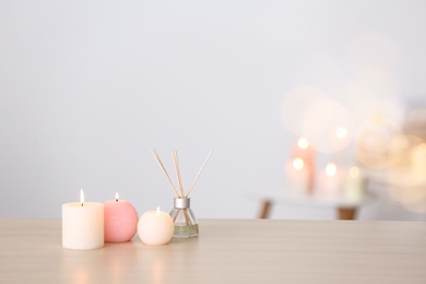 Candles and reed air freshener on table against blurred background, space for text. Spa concept