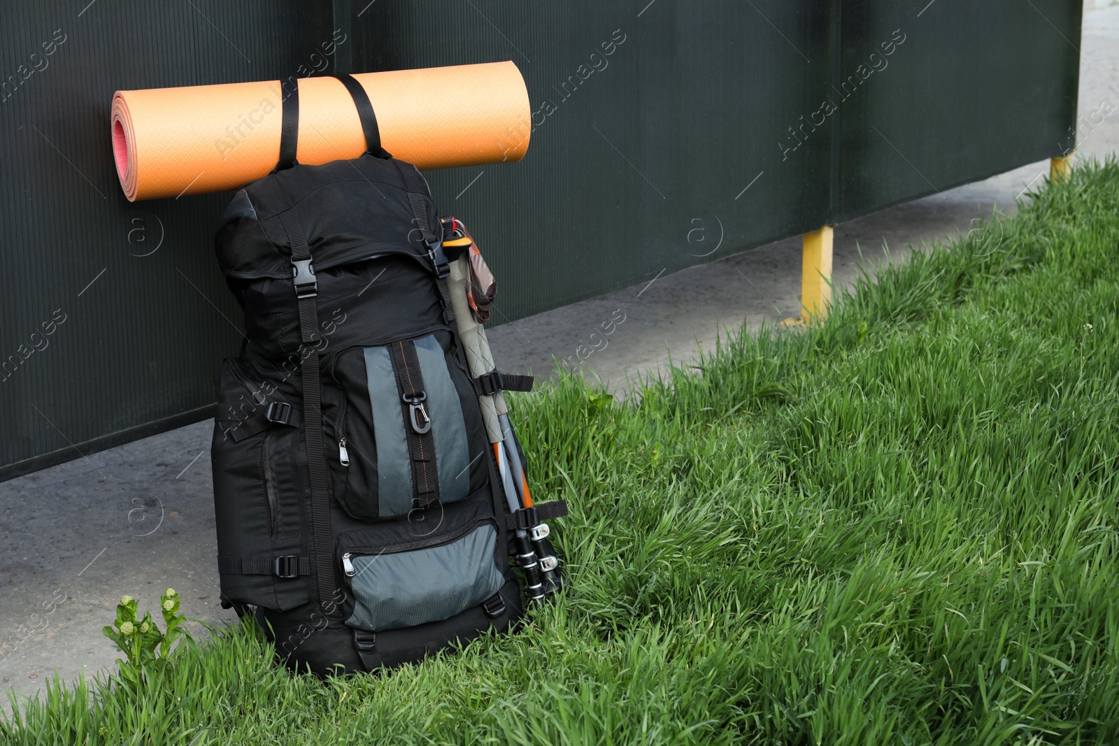 Photo of Backpack with trekking poles and camping mat on green grass. Space for text