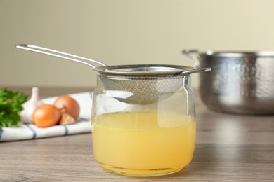 Photo of Straining delicious broth through sieve on wooden table
