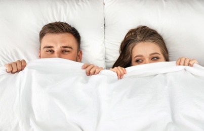 Photo of Young couple hiding under blanket together, top view. Bedtime