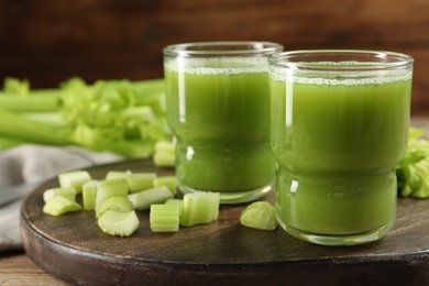 Photo of Glasses of delicious celery juice and vegetables on wooden board, closeup