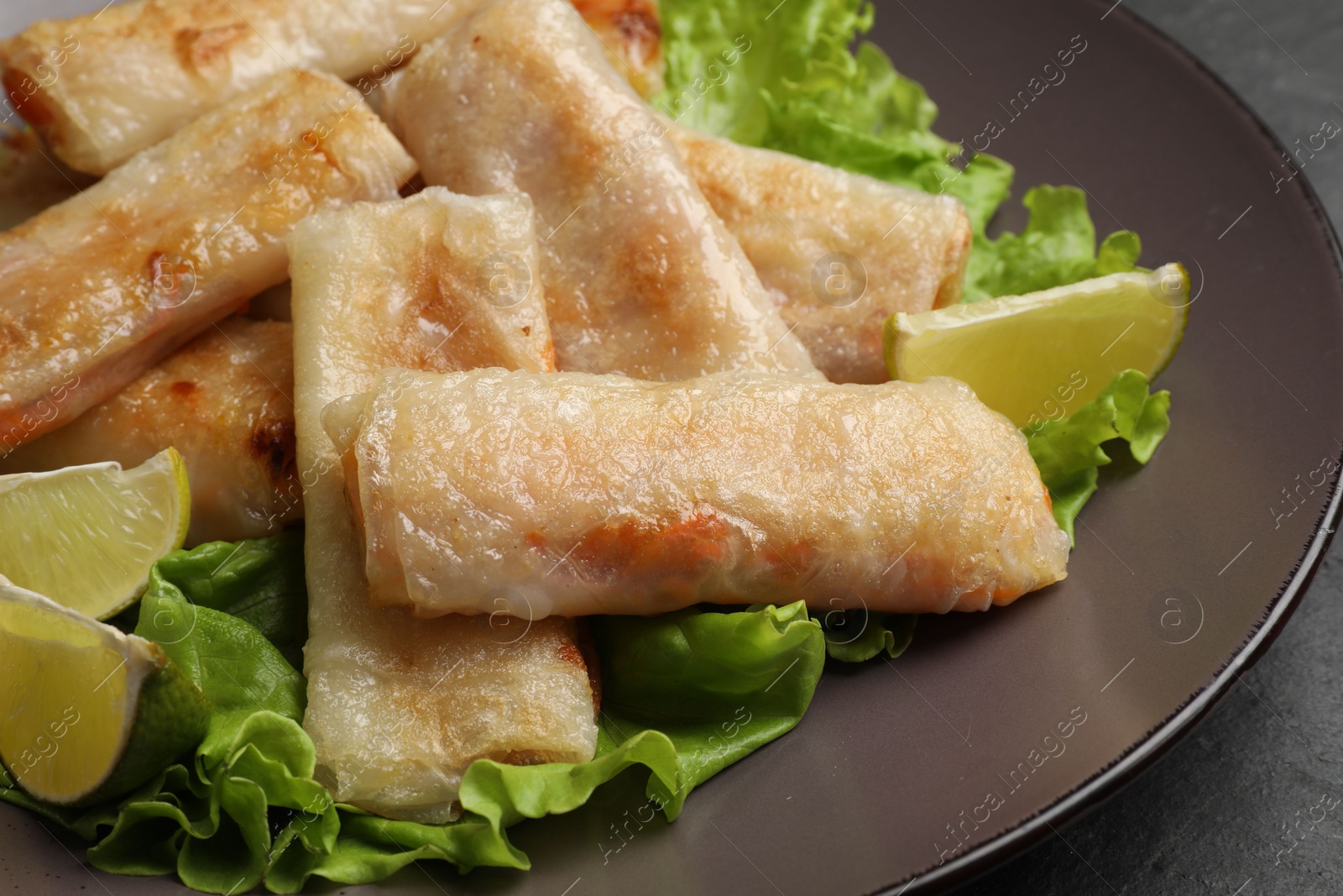 Photo of Plate with tasty fried spring rolls, lettuce and lime on dark table, closeup