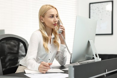 Secretary talking on phone and taking notes at table in office