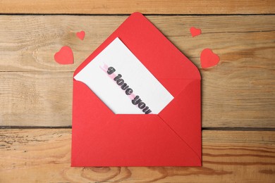 Photo of Card with phrase I Love You in envelope and paper hearts on wooden table, flat lay