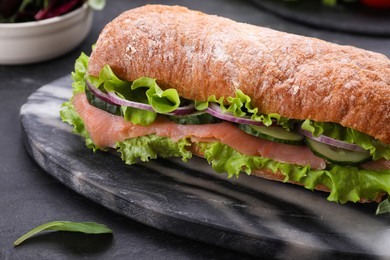 Photo of Delicious sandwich with fresh vegetables and salmon on black table, closeup