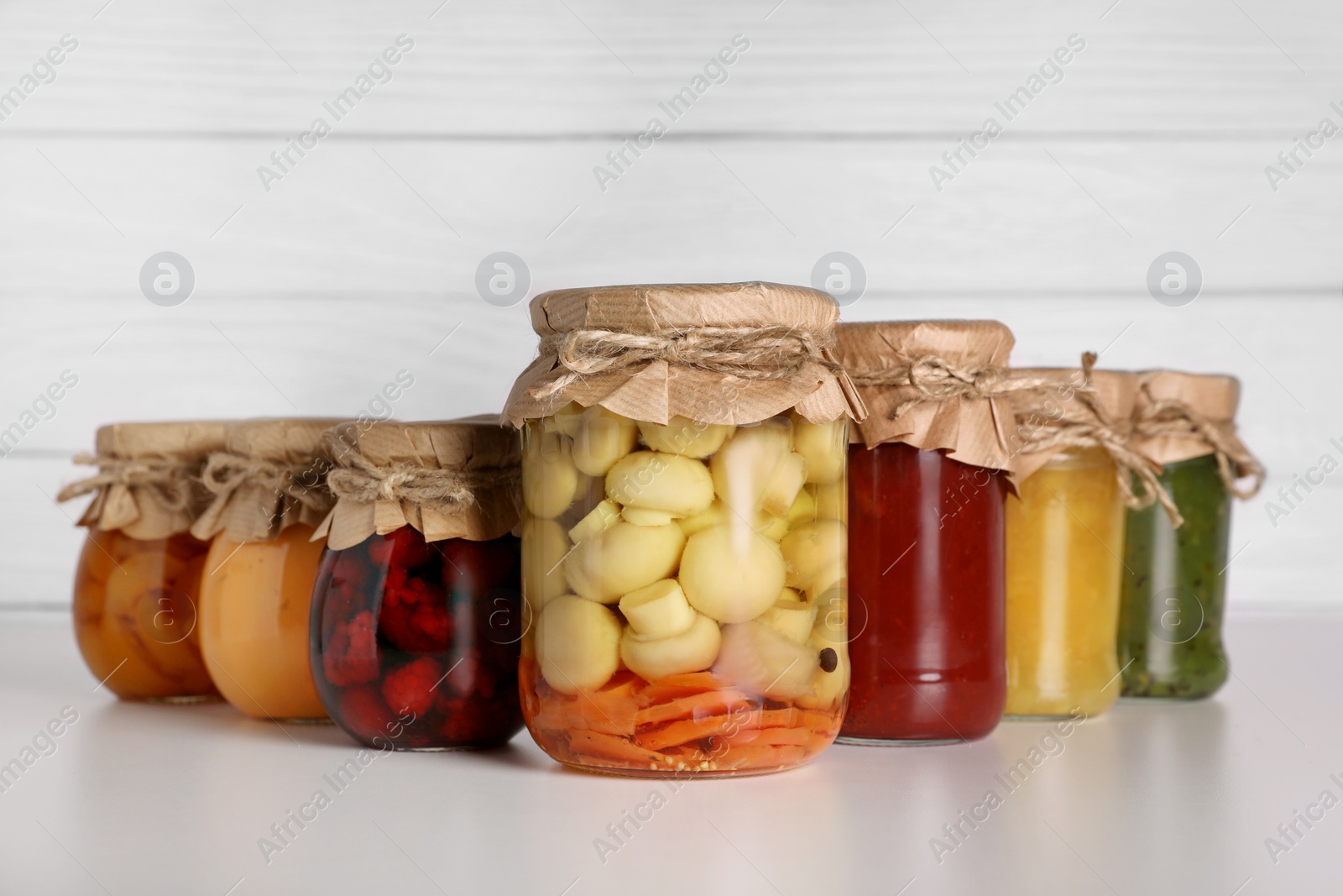 Photo of Many jars with different preserved products on light grey table