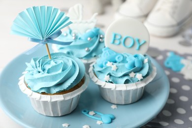 Photo of Delicious cupcakes with light blue cream and toppers for baby shower on table, closeup