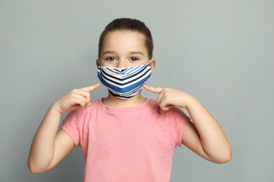 Photo of Cute little girl in protective mask on grey background