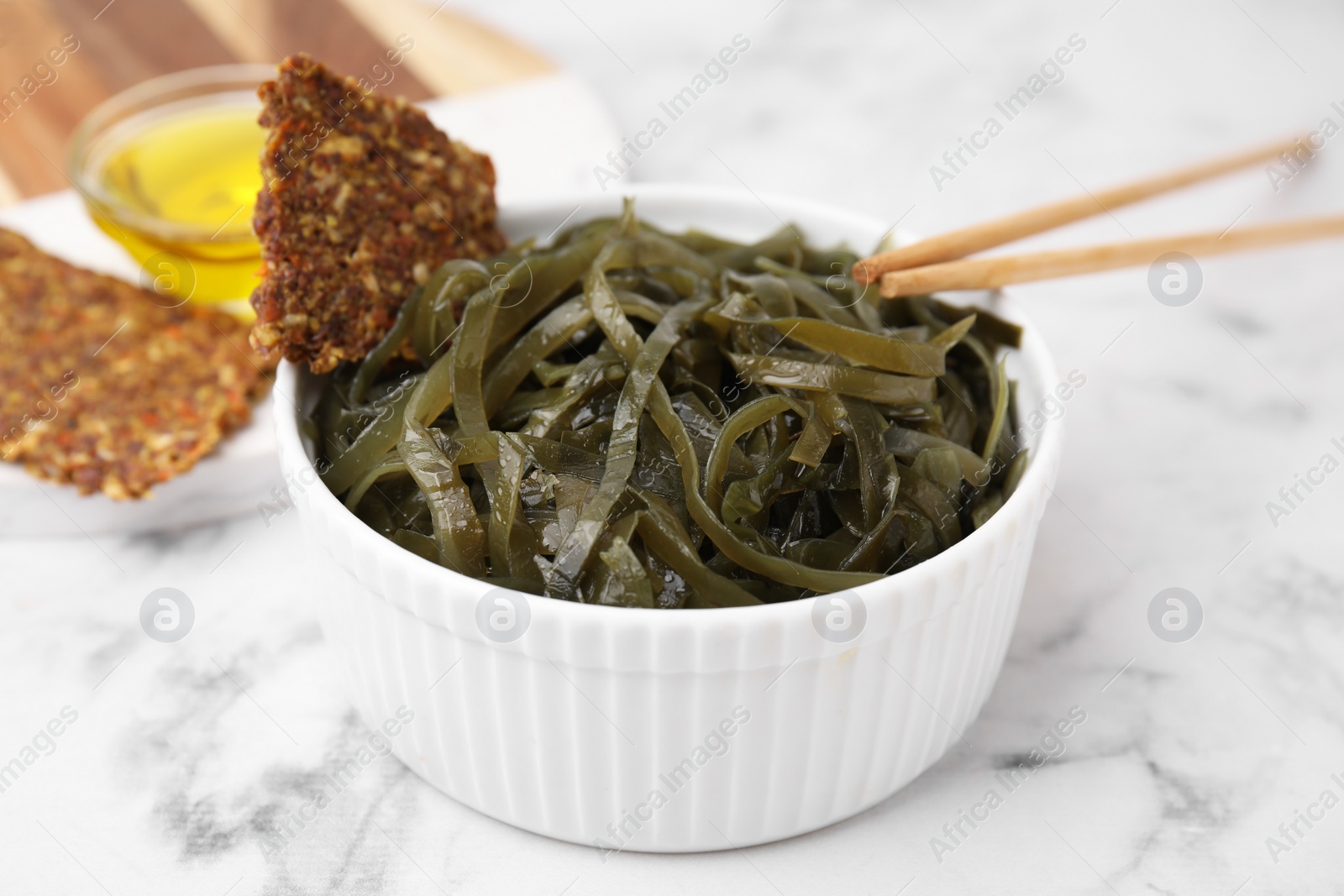 Photo of Tasty seaweed salad in bowl served on white marble table, closeup