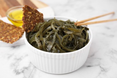 Photo of Tasty seaweed salad in bowl served on white marble table, closeup